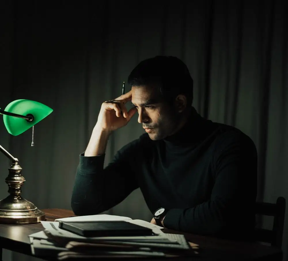Man zit 's avonds na te denken aan een bureau onder een lamp
