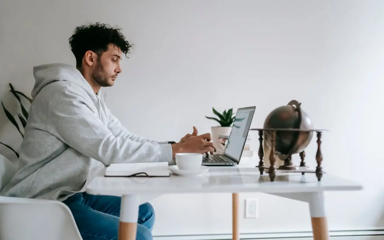 Man werkt aan een laptop aan een witte tafel